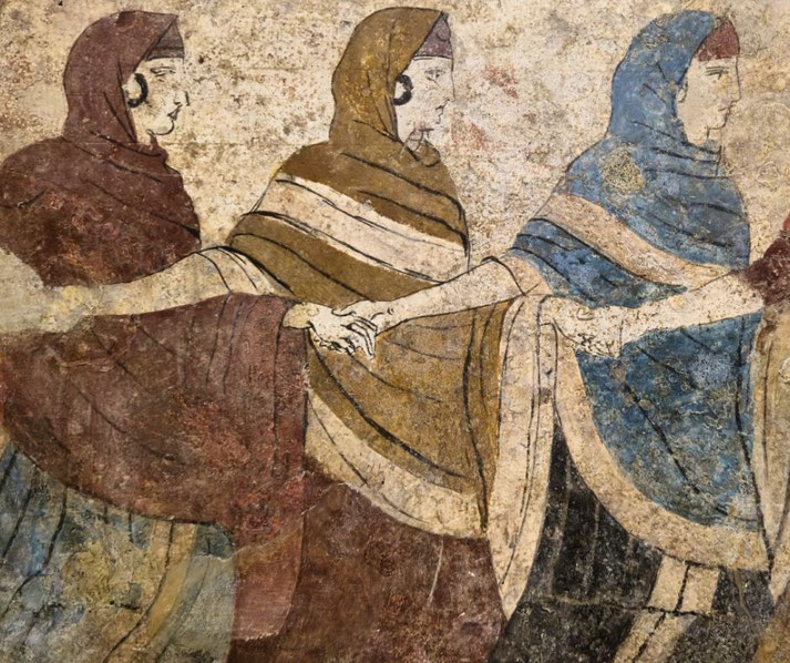 Ancient fresco showing four robed women in profile, holding hands in a line, wearing red, brown, and blue garments with head coverings and earrings.