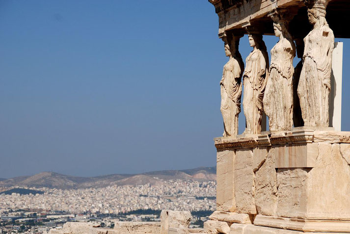 Statues of women as columns on the Erechtheion in Athens, overlooking the city and distant hills under a clear sky.