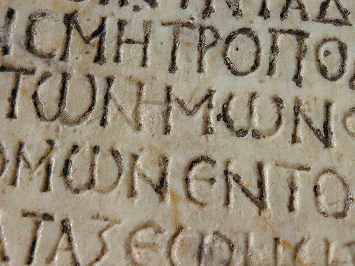 A close-up of ancient Greek inscriptions carved into stone, with weathered lettering that suggests historical significance and a connection to classical antiquity.