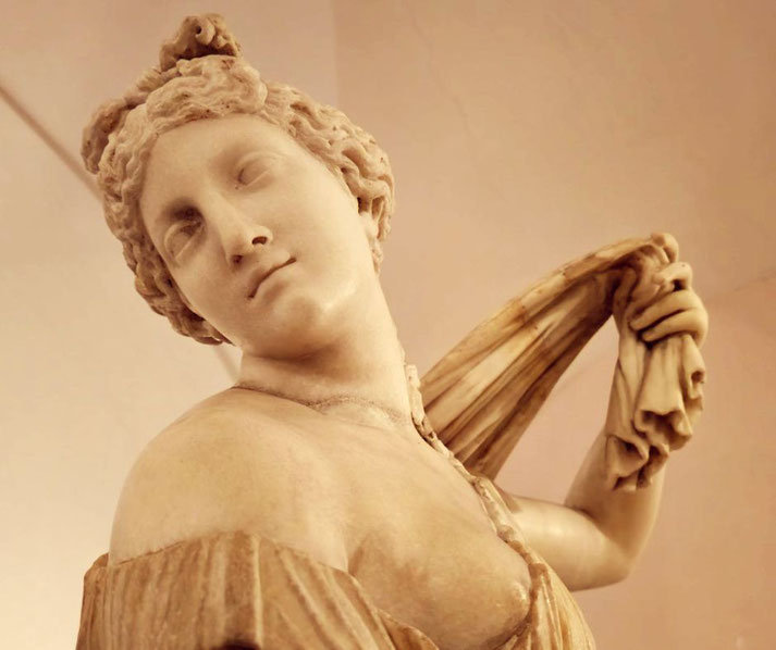 Marble statue of a graceful woman turning her head, holding draped fabric over her shoulder with a soft, serene expression.