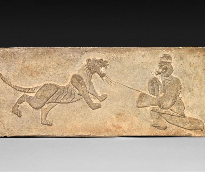 An ancient Chinese stone carving of a lancer facing a tiger. The figure kneels with a shield and spear.