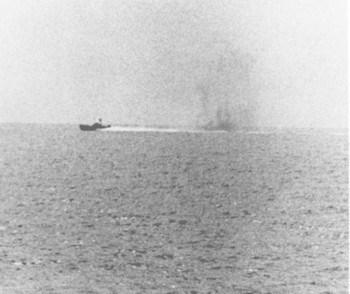 A small fast-moving torpedo boat speeds across open water, trailing a wake, with smoke rising from a distant impact.