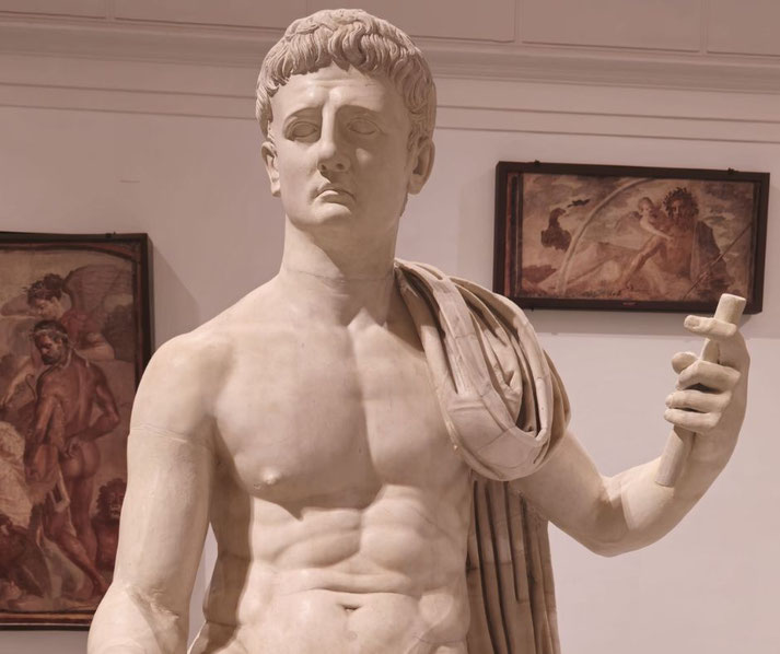 Marble statue of a Roman man with a draped cloak, holding a scroll and gazing sternly, symbolizing authority and intellect.
