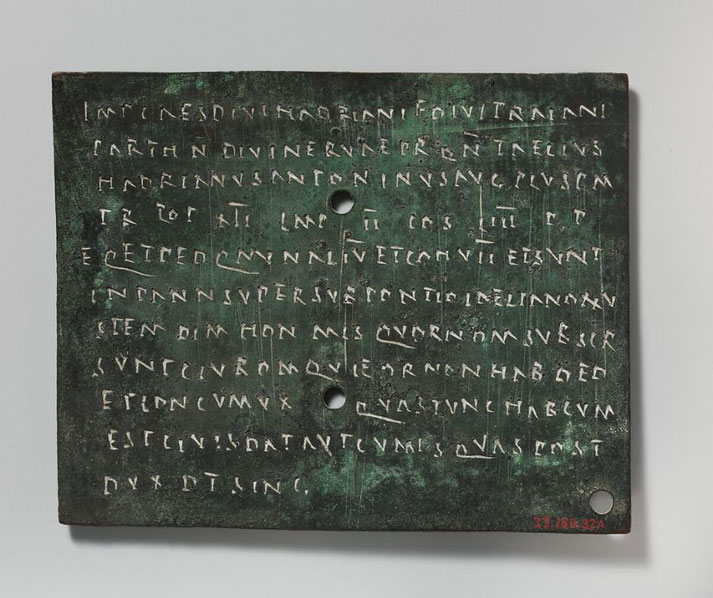 Ancient Roman bronze tablet inscribed with Latin text in capital letters, featuring multiple holes likely for mounting or binding.