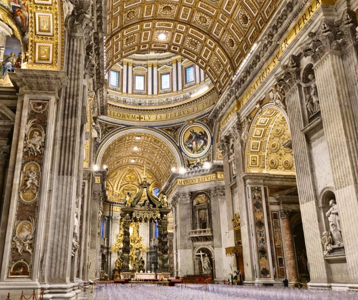 The grand interior of St Peter's Basilica in Rome, with intricate gold detailing, towering marble columns, and Bernini’s ornate baldachin beneath the massive dome.