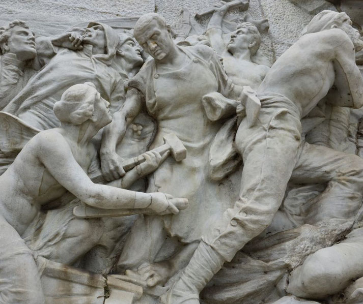 Dramatic marble relief showing workers and revolutionaries in motion, with tools in hand, symbolizing labor and struggle, carved in expressive detail.