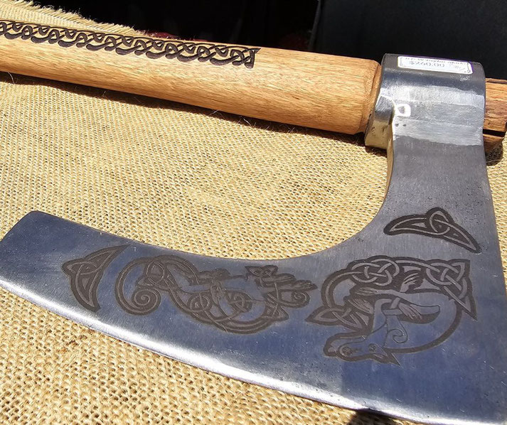 A decorative Viking-style axe with intricate Celtic engravings on the polished blade and a wooden handle adorned with knotwork designs.