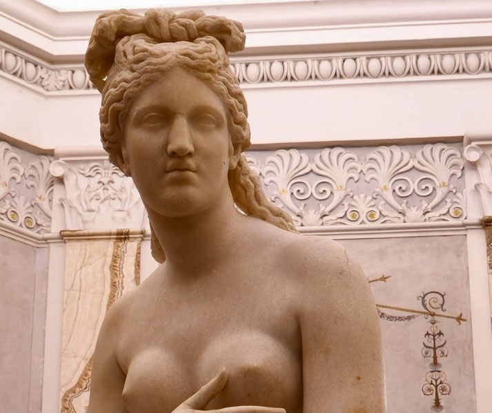 Close-up of a marble statue of a nude woman with a modest pose and detailed hair tied in a bow, likely representing the goddess Venus in a classical Roman style.