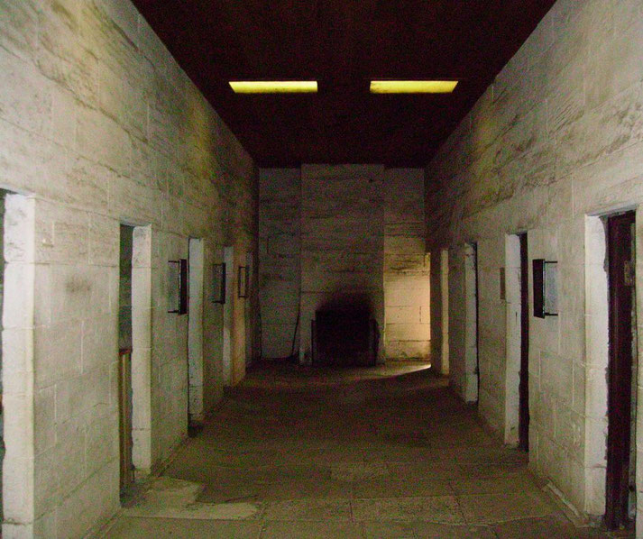 A dimly lit stone hallway with multiple doorways, possibly in an old prison or historical building. 