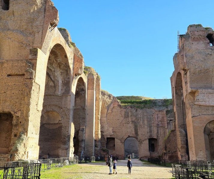 Massive ancient brick arches tower over visitors walking through a sunlit historic ruin.
