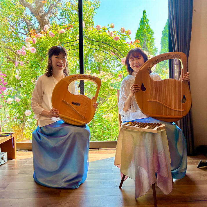 薔薇のアーチをバックに、ライアー奏者「リラ・コスモス」さん。右が発地美枝子さん、左が平川絵里子さん。