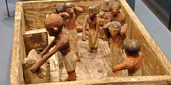 A wooden model depicting an ancient Egyptian granary, showing workers handling grain with detailed painted features. The miniature scene provides insight into daily labor and agricultural practices in ancient Egypt.