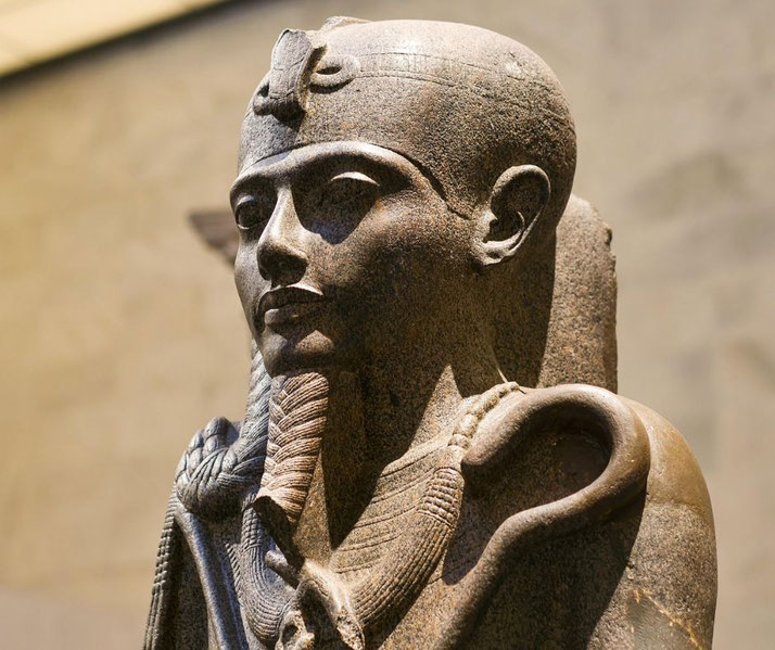A stone statue of a young Egyptian king, possibly Khonsu or a youthful pharaoh. He wears a royal headdress, a false beard, and holds a was-scepter, symbolizing power and divine authority.