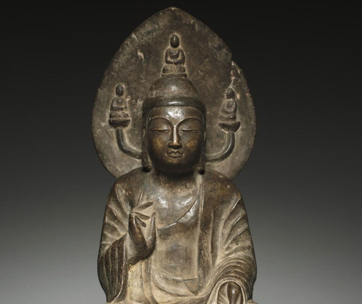 A bronze statue of Amida Buddha, seated in meditation with a serene expression. A mandorla behind him features three smaller Buddha figures.