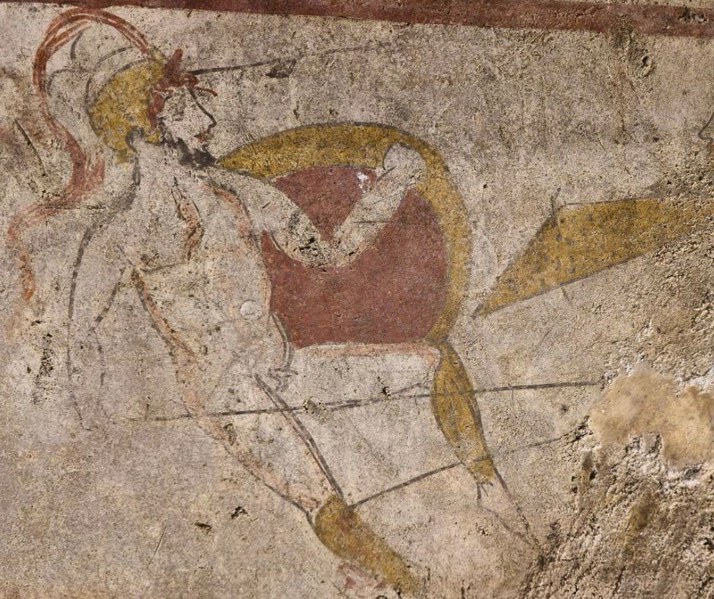 Faded wall painting of a warrior in motion with a red shield, yellow helmet, and spear, drawn in simple lines and earth tones.
