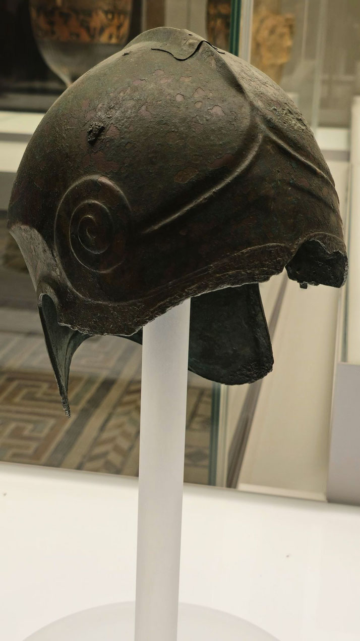 Bronze helmet with a distinct spiral design on the side and curved cheek guards, showing signs of age and wear.