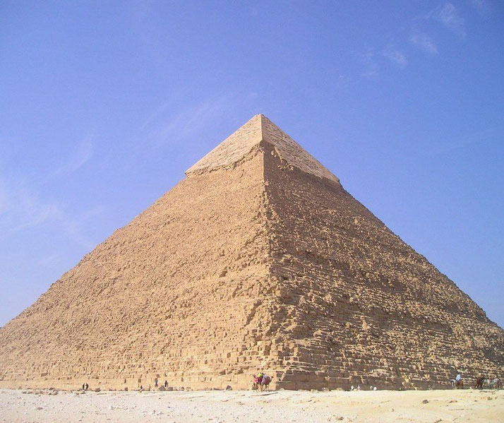 The Great Pyramid of Giza rises sharply under a clear blue sky, with tiny figures at its base showing its massive scale.