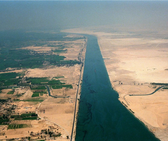 A wide canal cuts through desert terrain, with green farmland stretching along one side and barren sand on the other.