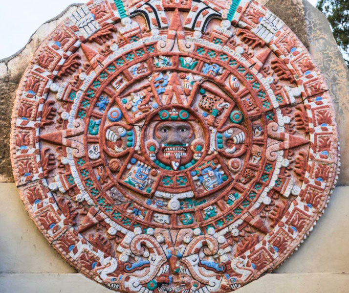 A colorful replica of the Aztec Sun Stone, featuring intricate carvings, geometric patterns, and vibrant red, blue, green, and white hues.