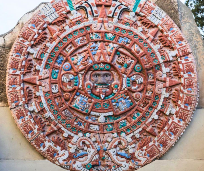 A colorful replica of the Aztec Sun Stone, featuring intricate carvings, geometric patterns, and vibrant red, blue, green, and white hues.