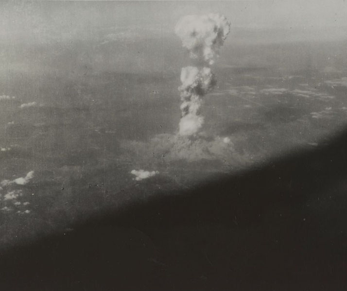 Aerial view of a large mushroom cloud rising over a city, captured moments after the detonation of an atomic bomb.