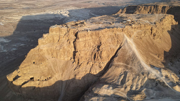 Aerial view of Masada, an ancient fortress atop a desert plateau, surrounded by arid terrain and steep cliffs.