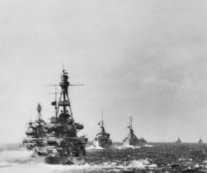 A formation of battleships and naval vessels sails through rough waters, captured in a historic black-and-white wartime photo.
