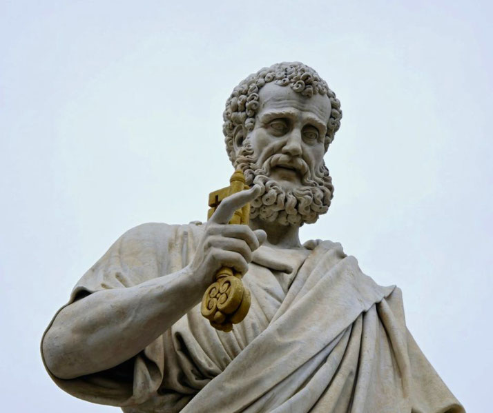 Marble statue of a bearded man in a robe holding a large golden key upright, symbolizing authority or guardianship.