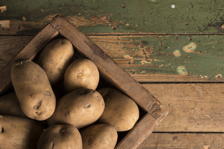Several raw potatoes sit in a wooden crate on a rustic wooden surface with peeling green paint.
