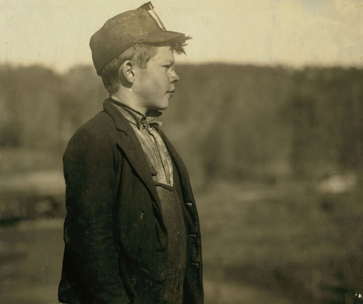 A young boy, likely a coal miner, wears a work cap with a lamp and worn clothing.