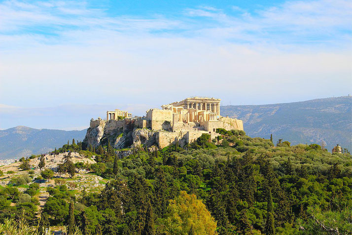 Distant view of the Acropolis of Athens, with the Parthenon prominently atop a rocky hill, surrounded by trees and mountains.