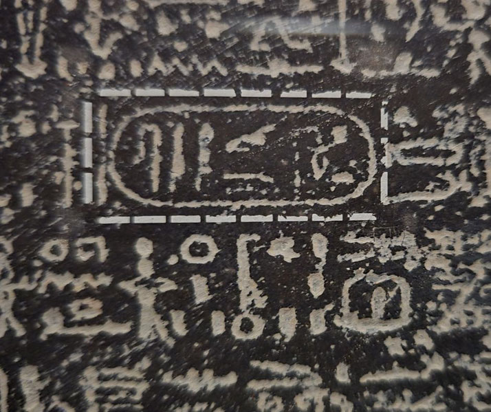 Ancient Egyptian hieroglyphs carved in stone, with a central cartouche enclosing royal symbols and glyphs.