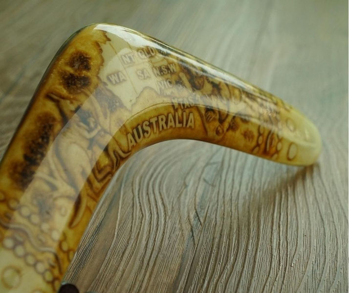 Close-up of a polished boomerang with Australia map artwork resting on a textured wooden surface.