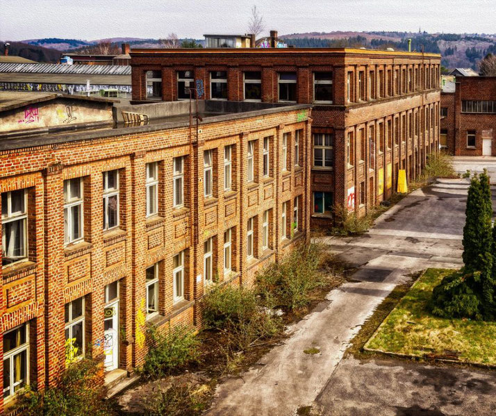 An abandoned brick building with overgrown plants around it. The structure shows signs of decay, with some graffiti on the walls and empty windows.