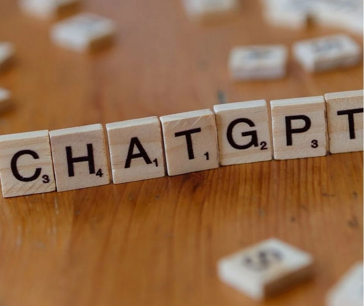 Wooden letter tiles arranged to spell ChatGPT on a wooden table, with scattered tiles blurred in the background and shallow depth of field.