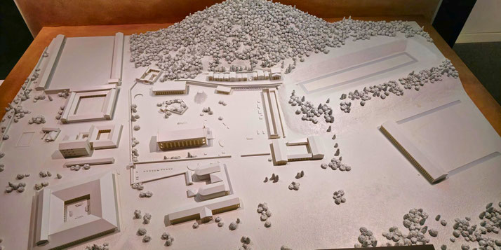 A detailed architectural model of ancient Olympia, featuring temples, buildings, and stadiums surrounded by trees. It represents the historic site of the ancient Olympic Games in Greece.