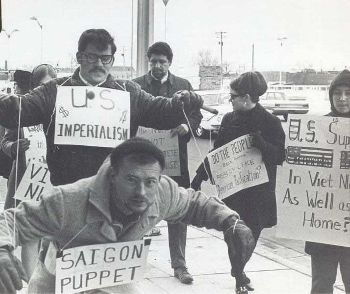 Protesters carry signs and act out "Saigon Puppet" demonstration in front of Wichita City Building.