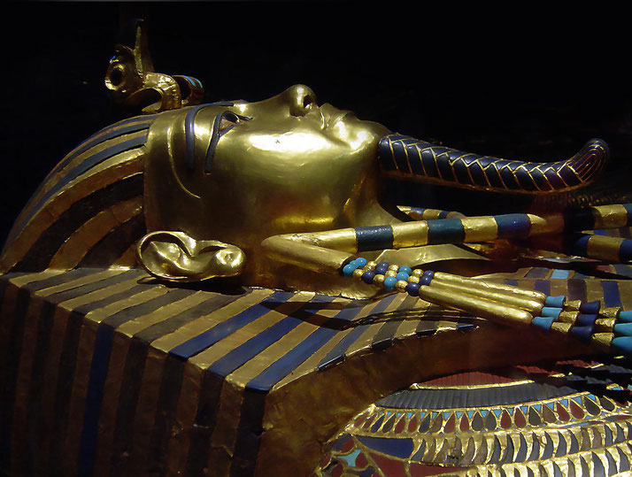 Close-up of King Tutankhamun’s gold burial mask with blue inlays, resting inside his decorated sarcophagus.