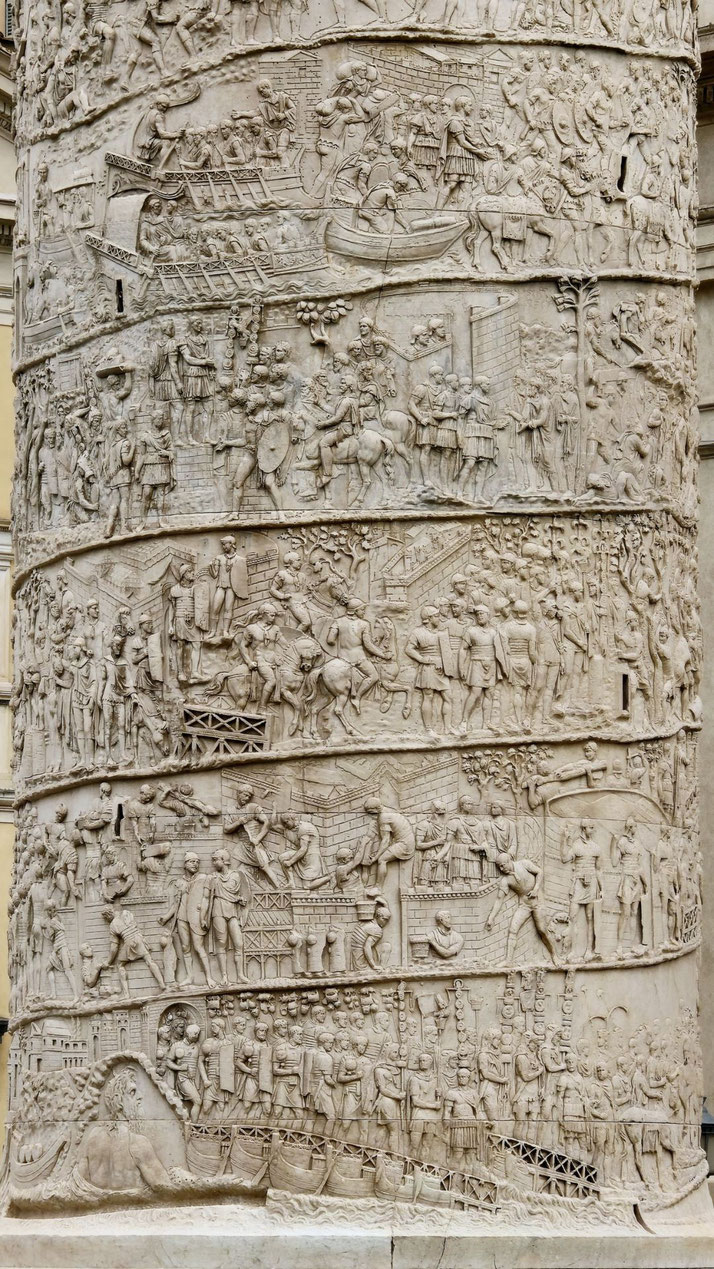 Detailed stone reliefs on a column depict Roman soldiers in battle, building structures, crossing rivers, and interacting with civilians in a continuous narrative spiral.