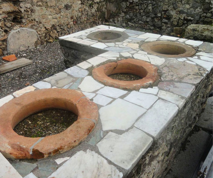 Ancient Roman countertop with embedded terracotta jars, part of a thermopolium used for serving hot food in Pompeii.