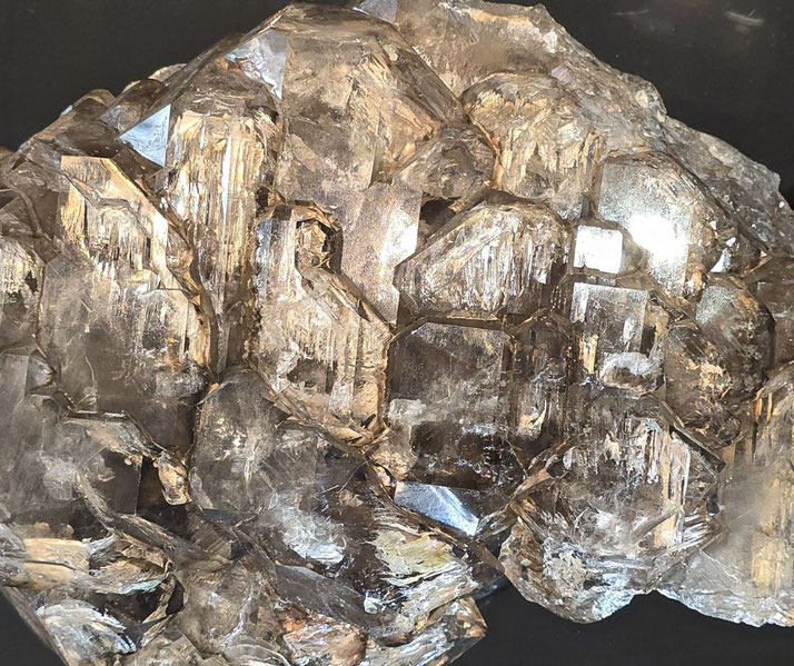Cluster of transparent, reflective crystals with angular, geometric facets and metallic luster on a dark background.