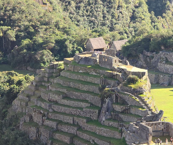 A close-up view of Machu Picchu's terraced stone structures, featuring steep agricultural terraces, stone stairways, and thatched-roof huts surrounded by lush green vegetation in the Andes Mountains.