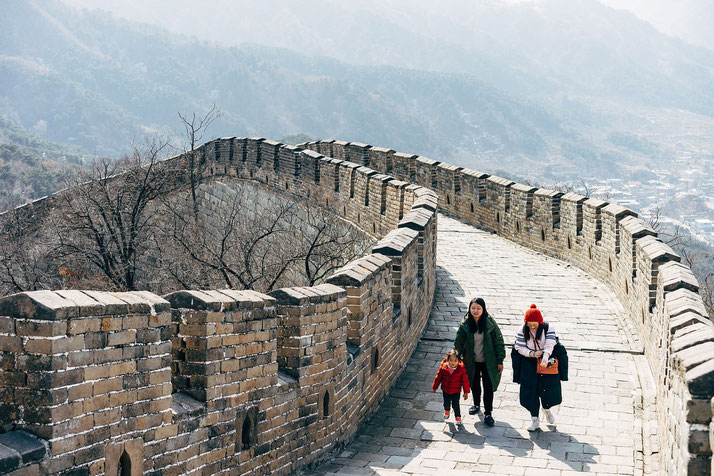 Three people walking along the Great Wall of China, surrounded by mountain scenery. 