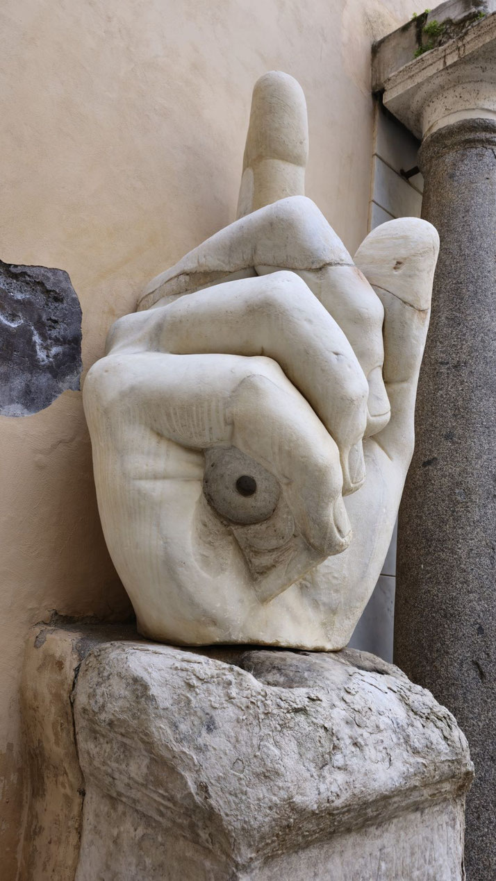 Massive marble sculpture of a right hand with the index finger pointing upward, resting on a stone pedestal.