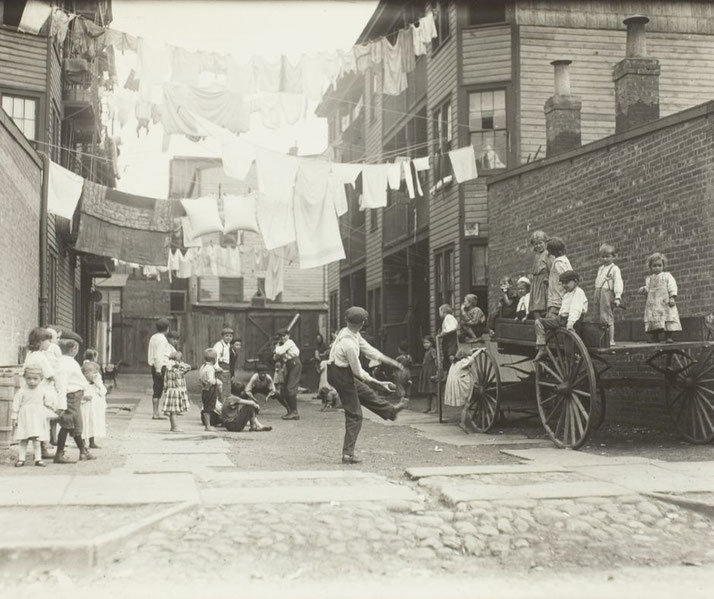 A black-and-white photo of children playing in a narrow alley, with clothes hanging on lines above.