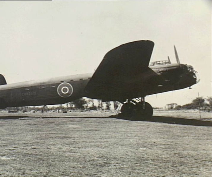 Side view of a British WWII bomber aircraft parked on a grassy airfield under clear skies.