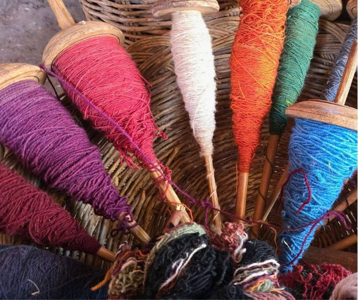 A collection of colorful yarn spools wound around wooden spindles, resting in a woven basket.