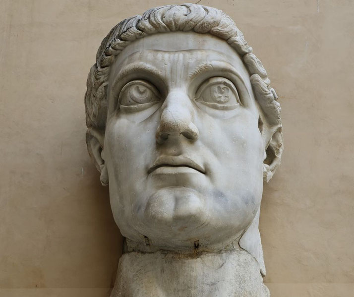 A massive marble head of a statue with large, wide eyes, a strong jawline, and wavy hair.