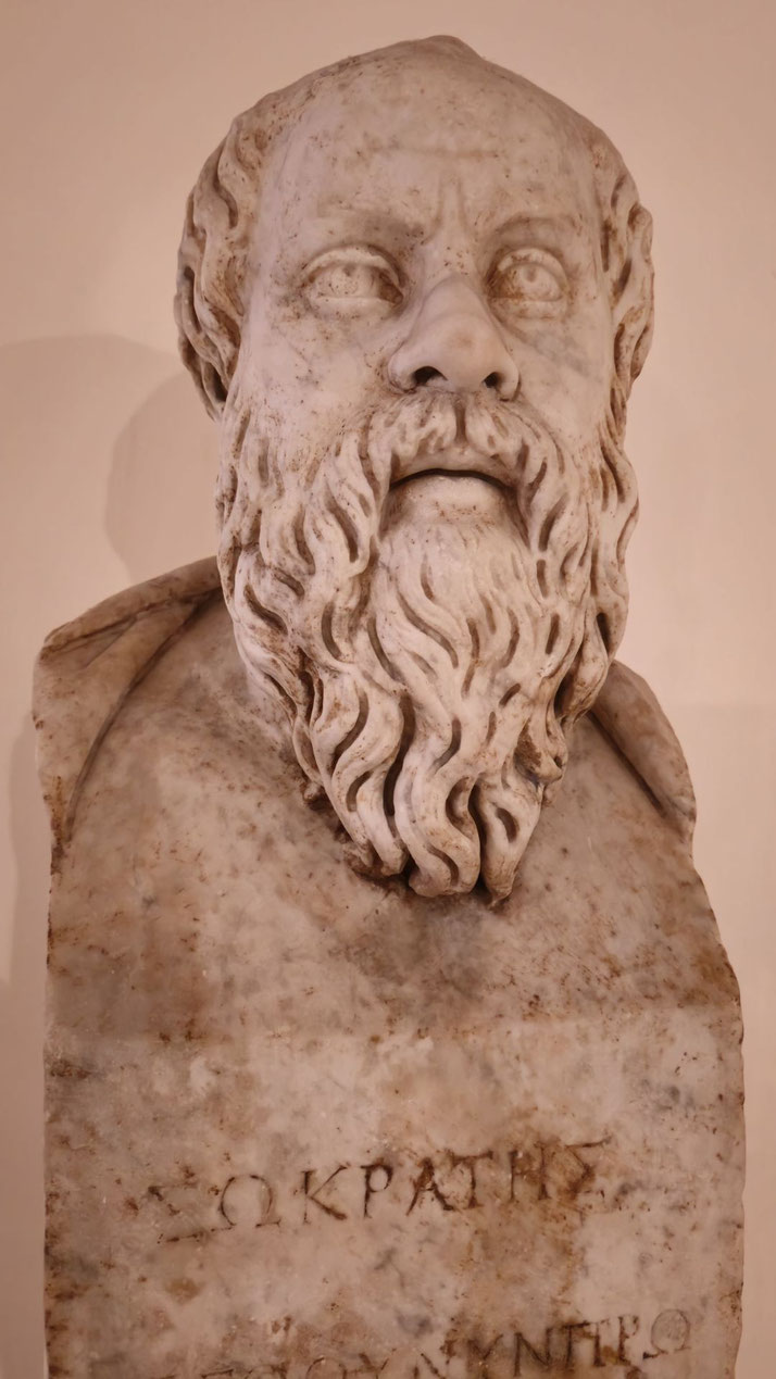 Marble bust of a bearded man with deep-set eyes and curly hair, featuring Greek inscriptions carved below on the base.