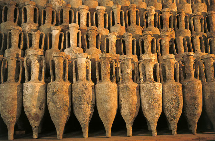 A tightly packed collection of ancient amphorae, showing weathered surfaces and uniform shapes, likely used for storage or transport in antiquity.